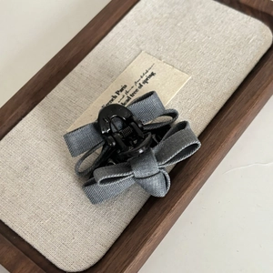 Detail of a gray twill fabric bow hair claw clip placed on a wooden tray accessory