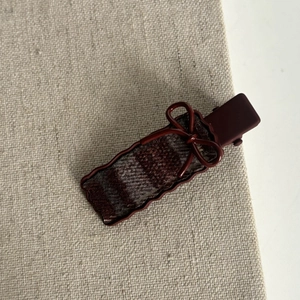 Detailed view of vintage red plaid hair clip with delicate bow on beige linen fabric