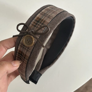 Close-up of brown plaid headband with leather bow and button accent detail