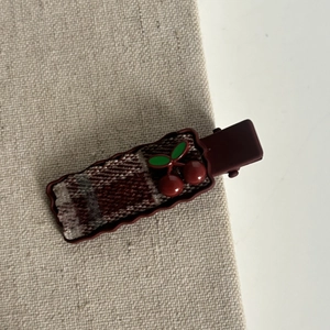 Detail of red plaid cherry bow hair clip featuring wavy edges and matte coffee-colored clamp