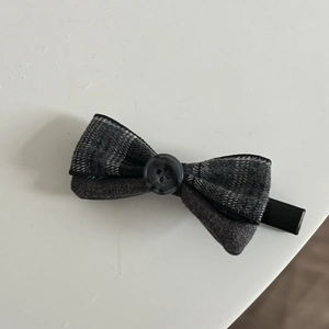 Detail of gray checkered bow hair clip with black button and metal alligator grip