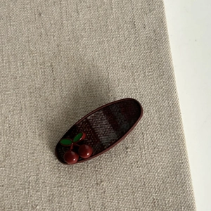 Retro red plaid hair clip with polished cherry accent on vintage beige linen background