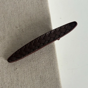 Détail d'une pince à cheveux tressée en cuir marron foncé sur un support en tissu