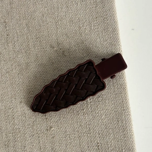 Détail d'une pince à cheveux marron foncé avec texture tressée sur lin neutre