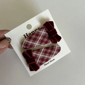 Close-up of two red plaid hair clips with velvet bows on a handmade display card