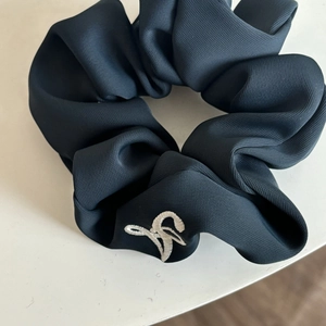 Detailed view of Prussian blue fabric scrunchie with white logo embroidery on textured cloth