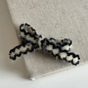 Close-up of a plush black and white checkered bow hair clip on a soft linen book cover