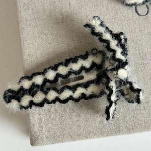 Handmade black and white wave knit hair clip with metal BB grip on grey linen background