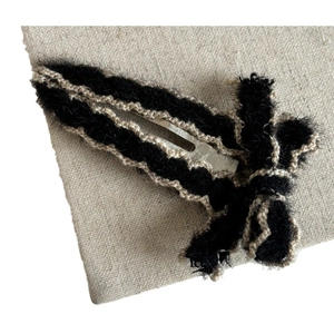 Elegant black faux fur bow hair clip with beige woven trim on natural linen background