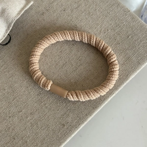 Détail d'un élastique à cheveux spirale tressé beige avec boucle mate sur tissu doux