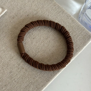 Élastique à cheveux marron avec texture tricotée en spirale et fermoir sur fond en lin