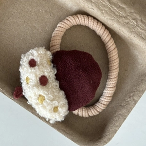 Dettaglio dell'elastico per capelli a fungo con texture sherpa crema e velluto bordeaux