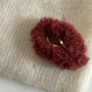 Gros plan détaillé d'une pince à cheveux en peluche rouge foncé sur tricot beige