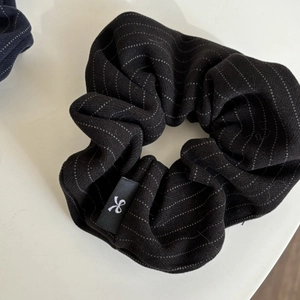 Striped black oversized scrunchie with white dots and brand logo label on white background