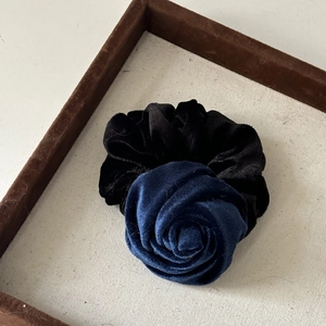 Close-up of a velvet rose hair tie in deep blue and black on a brown display tray