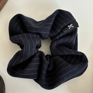 Detail of navy blue striped scrunchie featuring a fabric label with a white bow icon