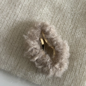 Gros plan sur une pince à cheveux en peluche beige avec clip doré sur tricot