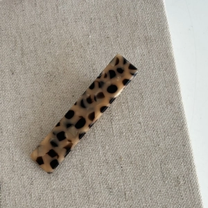 Detailed close-up of a French style leopard print hair clip on a beige textured background
