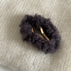 Gros plan d'une barrette à cheveux en peluche gris-violet sur fond tricoté blanc