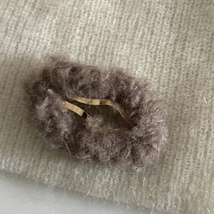 Détails de la pince à cheveux en peluche marron foncé sur fond tricoté beige