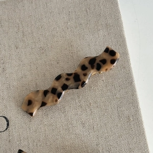 Detail of s-shaped leopard print hair clip on a textured linen background