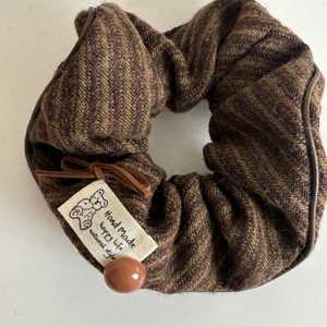 Macro shot of brown herringbone scrunchie with bear label, leather bow and button detail