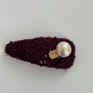 Detail of tweed hair clip with burgundy sequins, large pearl, and golden logo plaque