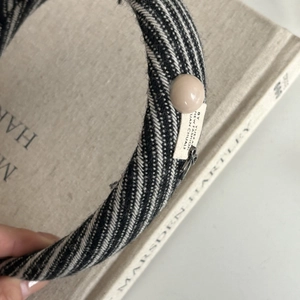Close-up of black and white twill headband with decorative pearl button and woven tag