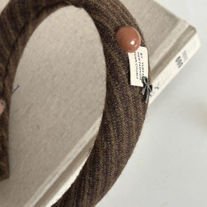 Detail of brown herringbone fabric headband with metal bow charm and decorative button