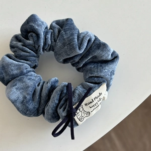Detailansicht eines blauen Samt-Haargummis mit schwarzer Schleife und Bärenstoffetikett