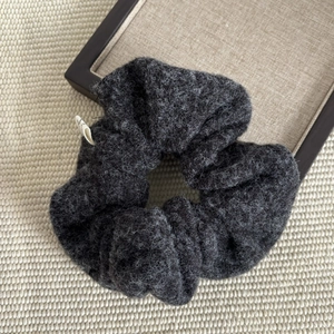 Macro detail of dark grey wool tweed scrunchie with soft fiber texture and small side label