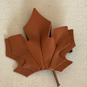 Autumn brown leather maple leaf hair clip with elegant stitching on beige fabric