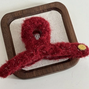 Elegant deep red plush hair claw clip with golden brand charm in a wooden display tray