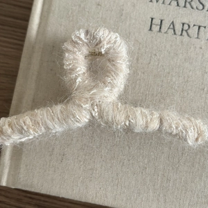 Gros plan d'une pince à cheveux en tricot beige sur un fond de livre en lin rustique