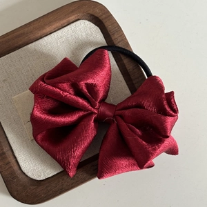 Macro shot of a wine red satin bow hair tie with elegant pleated texture on a wooden tray