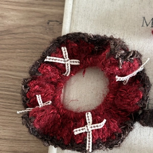 Détail d'un chouchou en crochet rouge et marron avec broderie de croix blanches en laine