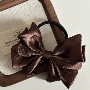 Macro shot of dark brown pleated satin bow hair tie with durable black elastic band