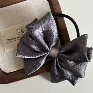 Close-up of a large silver pleated satin bow hair tie with a black elastic band