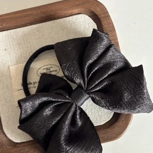 Detail of premium black satin bow hair tie with elegant pleated texture on a soft fabric mat