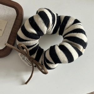 Close-up of black and white striped knit scrunchie with brown bow detail and label