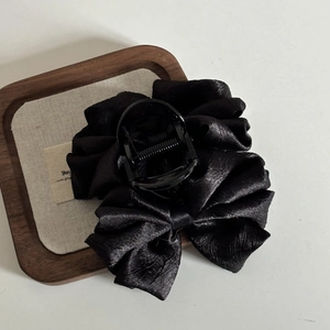 Detailed close-up of a large black satin bow shark hair claw clip with silk texture