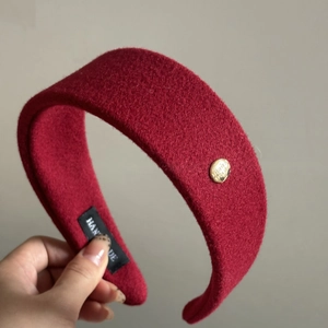 Close-up of handmade wide wool headband with golden logo plate and textured fabric