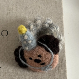 Detail einer handgefertigten Filz-Haarklammer mit süßem Gesicht und blauem Partyhut