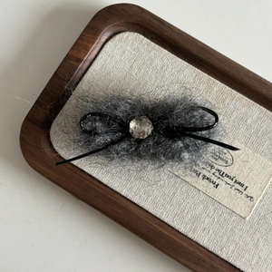 Barrette à cheveux avec nœud en peluche grise et diamant étincelant sur plateau bois