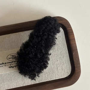 Minimalist black plush teddy fur hair clip accessory on a premium linen wooden tray