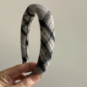 Detailed close-up of grey plaid padded headband with metallic logo and wool texture