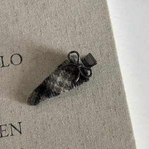 Close-up of a gray plaid fabric hair clip with a small black metal bow and textured detail