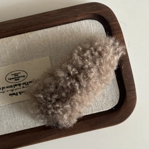 Detailed close-up of a plush taupe faux fur hair clip resting on a stylish wood display tray
