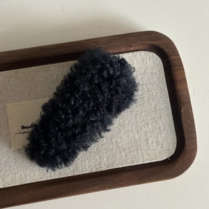 Close-up of a dark navy plush teddy fur hair clip on a wooden tray with linen texture