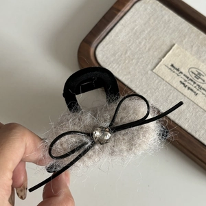Détail d'une pince à cheveux en peluche avec fourrure grise, nœud et perle en cristal